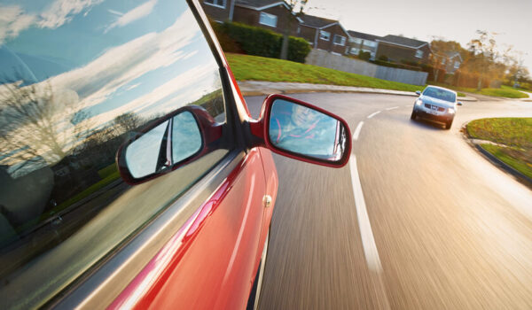 A man driving a red car towards a bend in the road.