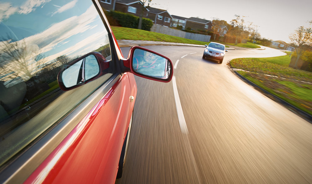 A man driving a red car towards a bend in the road.