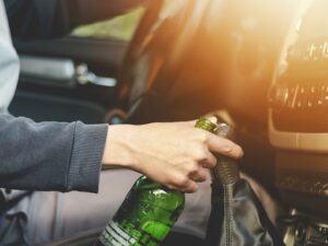 driver holding a bottle of alcoholic drink while driving