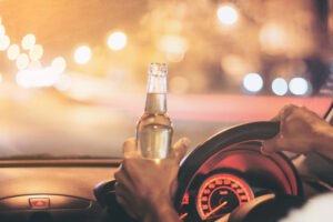 young man drives a car with a bottle of beer.